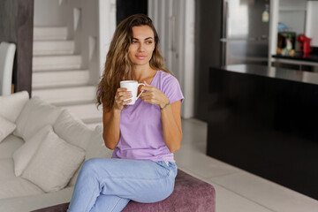 Beautiful pretty brunette woman resting in living room,  drink tea  and sitting on cozy sofa. Modern lifght  interior.