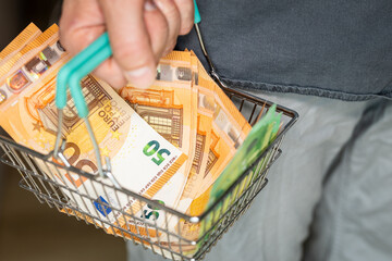euro money in shopping cart. A man holding a basket in his hand filled to the brim with 50 euro...