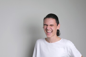 Laughing guy. Happy laughing face. Teenager with dark long hair in a white T-shirt