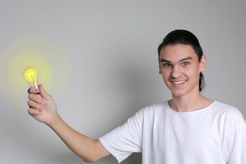 Young man smiling and holds glowing light bulb in his hand