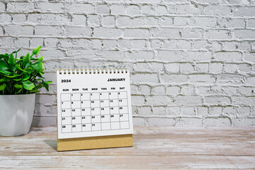 White January 2024 calendar on office wooden desk with potted plant.