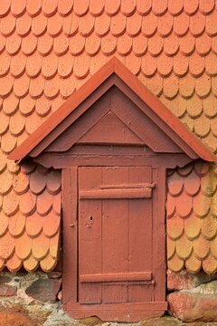 Red wooden door with wooden red shingle roof nearly reaching the ground.