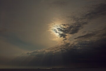 Sun behind clouds at seashore in spring weather.