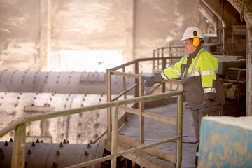 A worker in a helmet and equipment stands against the backdrop of a cement plant workshop. Work technology, cement production. People working in heavy industry.