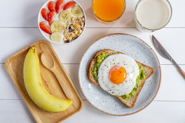 Healthy Breakfast food. Avocado toast with fried egg and bowl of yogurt with granola ,banana,...
