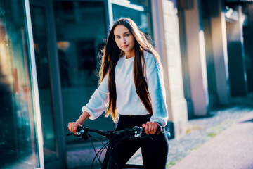 A smiling young woman rides a bicycle through the city streets.