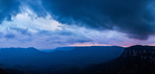 Dramatic stormy sky over layered blue mountains at nightfall