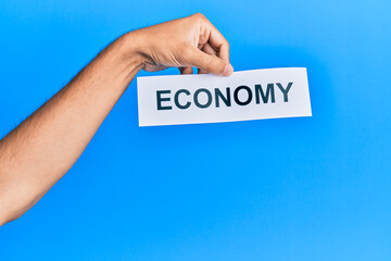 Hand of caucasian man holding paper with economy word over isolated blue background