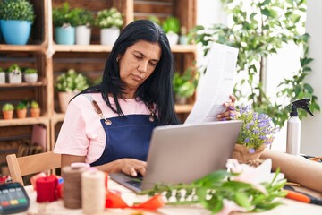 Middle age hispanic woman florist using laptop reading document at florist