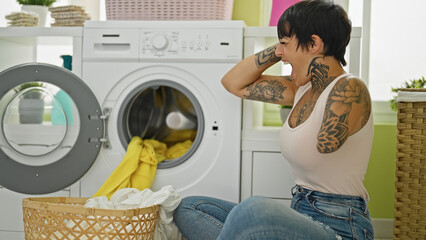 Hispanic woman with amputee arm washing clothes sitting on floor stressed at laundry room