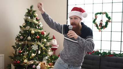 Young redhead man singing song and dancing by christmas tree at home