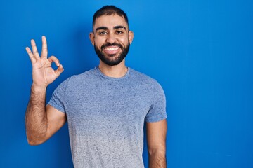 Middle east man with beard standing over blue background smiling positive doing ok sign with hand and fingers. successful expression.
