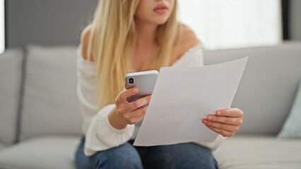 Young blonde woman reading document using smartphone at home