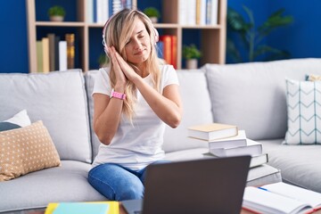 Obraz premium Young blonde woman studying using computer laptop at home sleeping tired dreaming and posing with hands together while smiling with closed eyes.