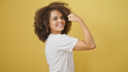 Young beautiful hispanic woman smiling confident doing strong gesture with arm over isolated yellow...