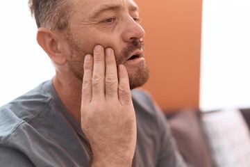 Fototapeta premium Middle age man suffering for toothache sitting on sofa at home