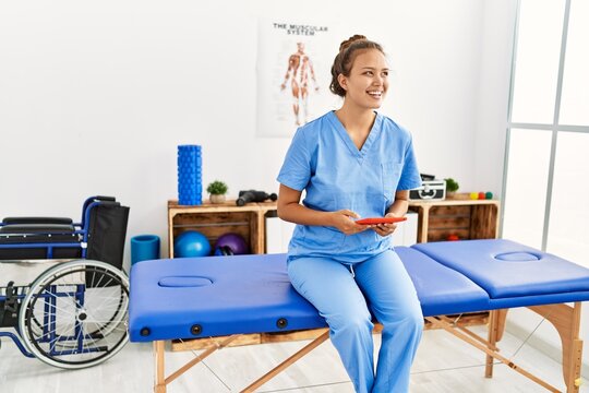 Young beautiful hispanic woman physiotherapist smiling confident using touchpad at rehab clinic