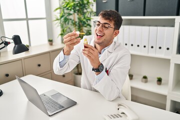 Young hispanic man optician smiling confident holding medication bottle at clinic