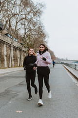 Two girls or hispanic couple of women in sports outfit running and doing exercises outdoors in winter weather in european city