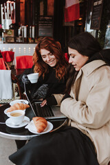 hispanic business couple of women working and using laptop at coffee shop in winter in an urban city in Europe