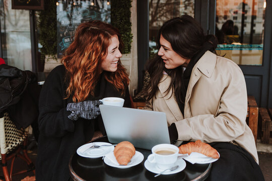 hispanic business couple of women working and using laptop at coffee shop in winter in an urban city in Europe