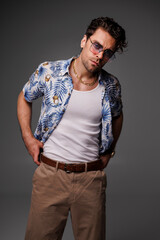 Good looking man in sunglasses, tank top and aloha shirt posing isolated on grey 
