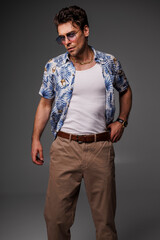 Well dressed man in aloha shirt, sunglasses and tank top posing isolated on grey 
