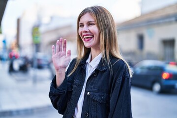 Young blonde woman smiling confident saying hello with hand at street