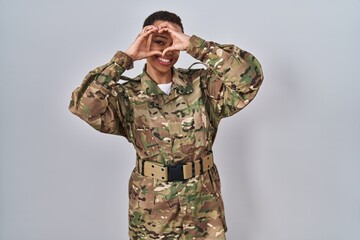 Beautiful african american woman wearing camouflage army uniform doing heart shape with hand and fingers smiling looking through sign