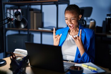 Beautiful african american woman working at the office at night shouting with crazy expression doing rock symbol with hands up. music star. heavy concept.