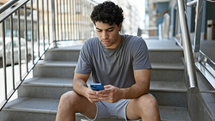 Young latin man using smartphone with serious expression at street