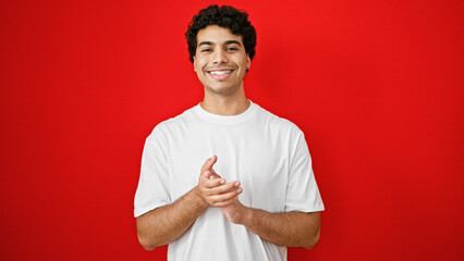 Young latin man smiling confident clapping over isolated red background