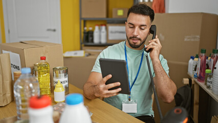 Young arab man volunteer using touchpad talking on telephone at charity center