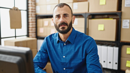 Young hispanic man ecommerce business worker using computer with serious face at office