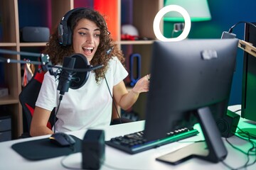 Hispanic woman with curly hair playing video games celebrating achievement with happy smile and...