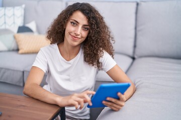 Young beautiful hispanic woman using touchpad sitting on floor at home