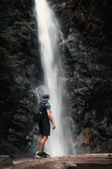 Young man hiker with a backpack standing on a cliff of a waterfall