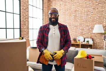 African american man working at home renovation looking positive and happy standing and smiling...