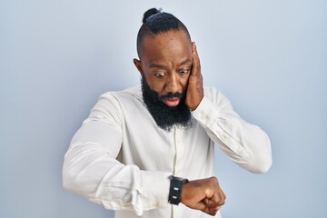African american man standing over blue background looking at the watch time worried, afraid of...