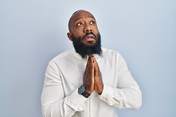 African american man standing over blue background begging and praying with hands together with...
