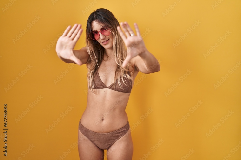 Canvas Prints young hispanic woman wearing bikini over yellow background doing frame using hands palms and fingers