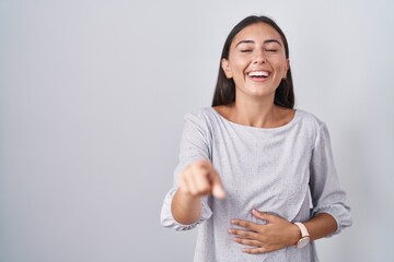 Young hispanic woman standing over white background laughing at you, pointing finger to the camera...