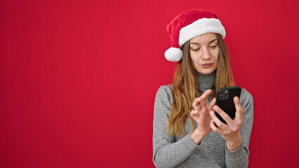 Young caucasian woman wearing christmas hat using smartphone over isolated red background