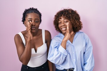 Obraz premium Two african women standing over pink background hand on mouth telling secret rumor, whispering malicious talk conversation