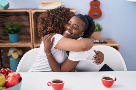 African american women mother and daughter hugging each other drinking coffee at home