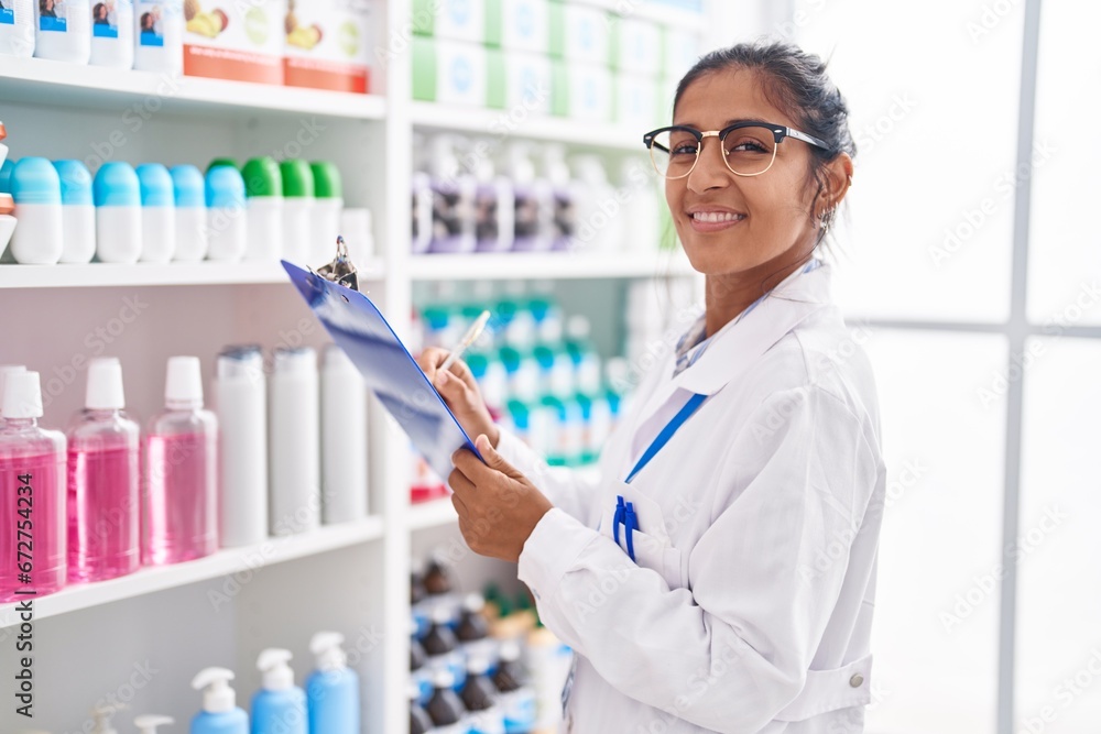 Sticker Young beautiful hispanic woman pharmacist writing on document at pharmacy