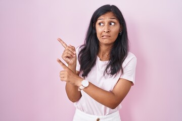 Young hispanic woman standing over pink background pointing aside worried and nervous with both...