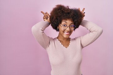 Young african american woman standing over pink background posing funny and crazy with fingers on head as bunny ears, smiling cheerful