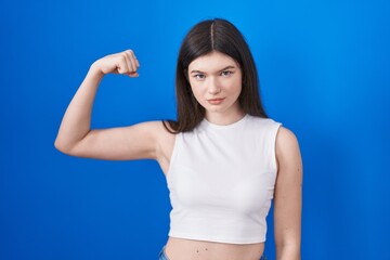 Fototapeta na wymiar Young caucasian woman standing over blue background strong person showing arm muscle, confident and proud of power