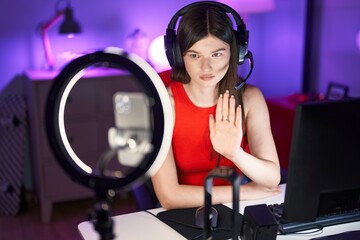 Young caucasian woman playing video games recording with smartphone with open hand doing stop sign with serious and confident expression, defense gesture